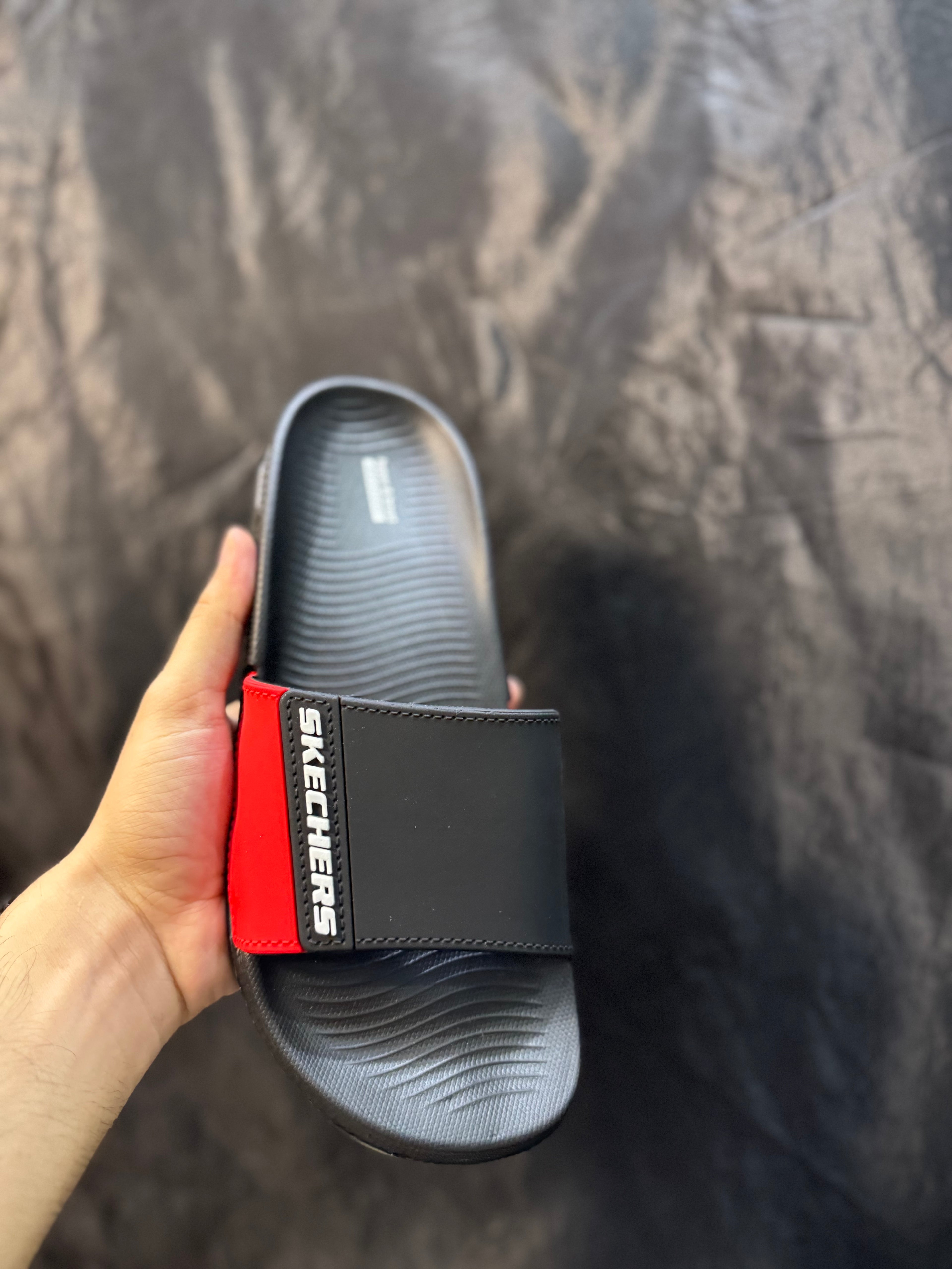 Black slide sandal with red and white logo held against a dark background